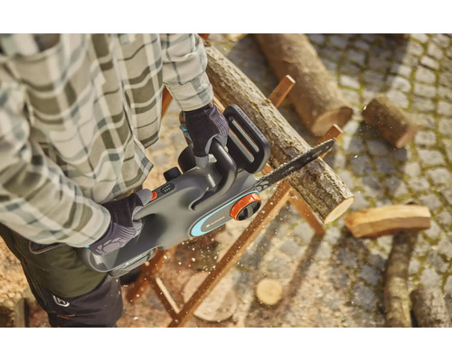 Un homme scie du bois avec une tronçonneuse à batterie Gardena.