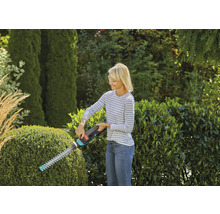 Femme taillant une haie avec un taille-haie dans le jardin.