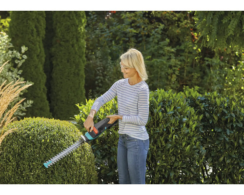 Frau schneidet Hecke mit Heckenschere im Garten.