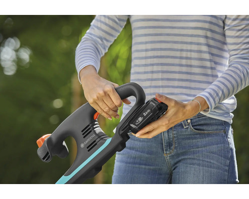 Frau setzt einen Akku in einen Gardena Rasentrimmer ein