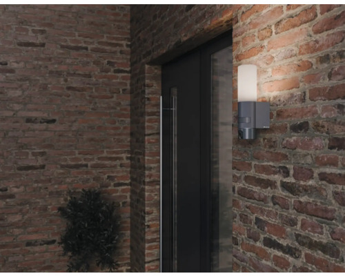 Außenwandleuchte mit Bewegungsmelder an einer Ziegelmauer neben einer Tür.