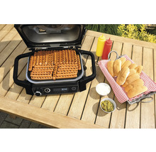 Gril électrique avec saucisses sur une table de jardin avec des ingrédients