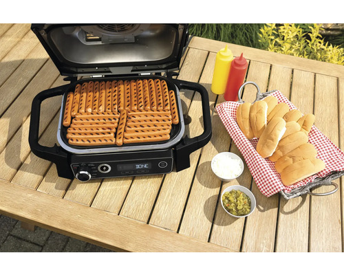 Elektrogrill mit Würstchen auf einem Gartentisch mit Zutaten