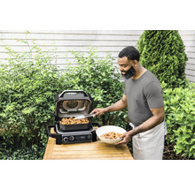 Un homme prépare un repas avec un barbecue Ninja dans le jardin.