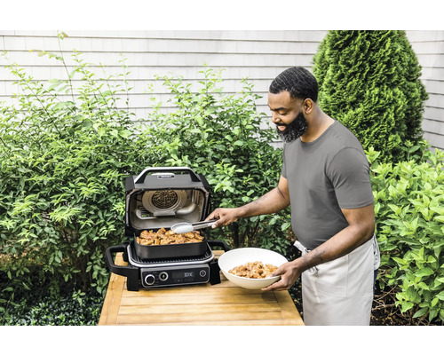 Mann bereitet Mahlzeit mit einem Ninja Grill im Garten zu.