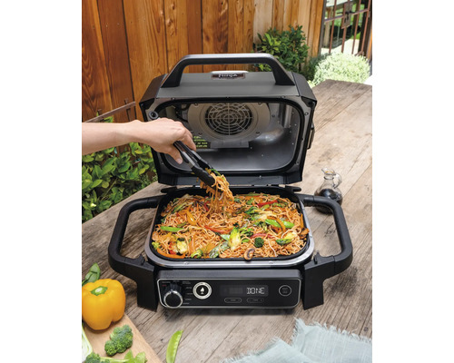 Elektrogrill mit Gemüse und Nudeln auf einem Holztisch