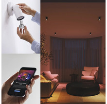 Mise en scène : une personne change une ampoule dans un applique murale, smartphone avec commande d’application, salon avec plafonniers.