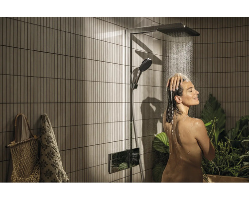 Frau unter einer Duscharmatur mit Kopfbrause und Handbrause in einem Badezimmer mit Pflanzen.