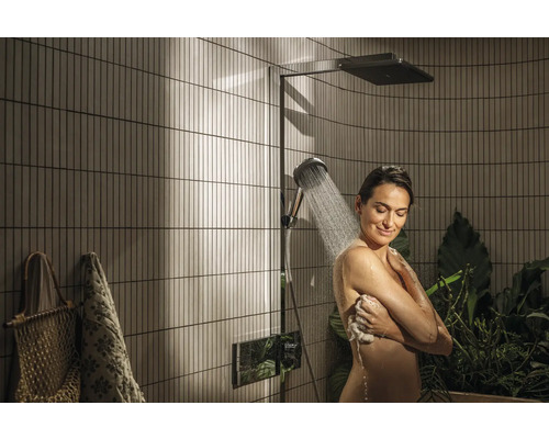 Eine Frau duscht unter einer Duschgarnitur in einem Badezimmer mit vertikalen Fliesen.