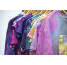 Des t-shirts multicolores avec un motif batik sont suspendus à une tringle à vêtements.