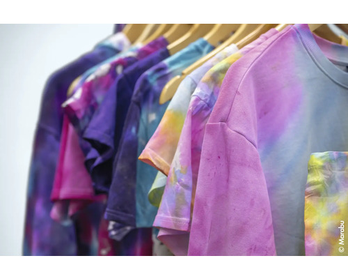 Des t-shirts multicolores avec un motif batik sont suspendus à une tringle à vêtements.