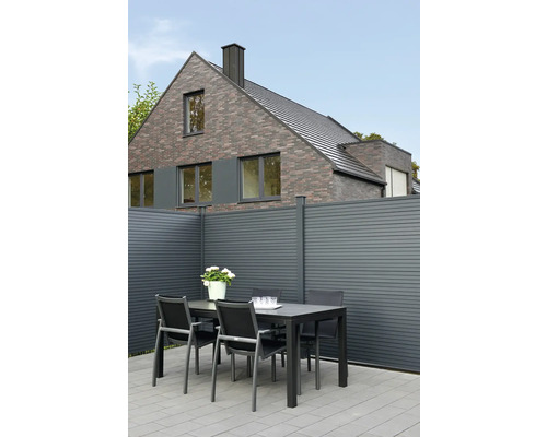 Scène de jardin avec table, chaises et clôture devant une maison d'habitation.