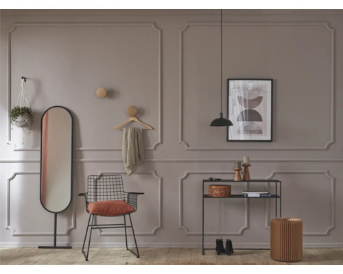 Wohnraum mit Spiegel, Stuhl, Regal und dekorativen Elementen vor einer Wand mit Zierleisten