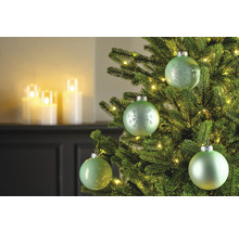 Nahaufnahme eines Weihnachtsbaums mit grünen Kugeln und Lichtern, im Hintergrund Kerzen.
