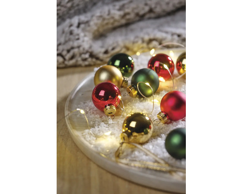 Dekorative Weihnachtskugeln auf einem Teller mit Kunstschnee und Lichterkette