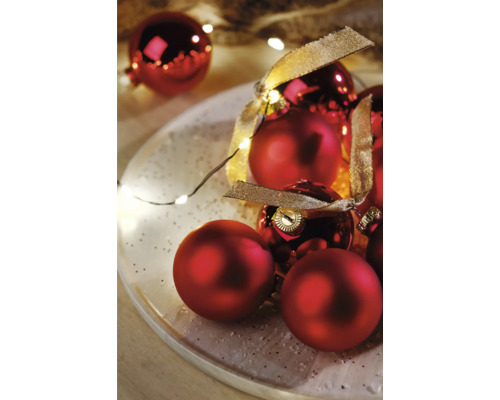 Boules de Noël rouges avec ruban sur une assiette avec guirlande lumineuse