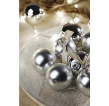 Dekorative Christbaumkugeln mit glänzender Oberfläche und Schleifen auf einem Teller