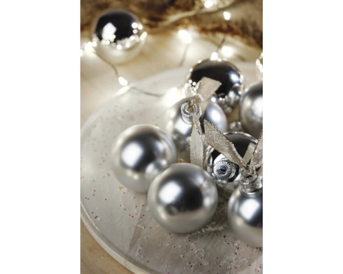 Dekorative Christbaumkugeln mit glänzender Oberfläche und Schleifen auf einem Teller