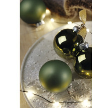 Dekorative Weihnachtskugeln auf einem Teller mit Kunstschnee und Lichterkette