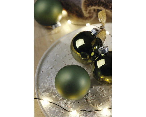 Dekorative Weihnachtskugeln auf einem Teller mit Kunstschnee und Lichterkette