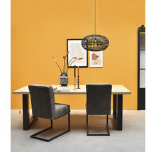 Coin repas moderne avec table en bois, pieds noirs en U, deux chaises grises et suspension noire en métal devant un mur jaune.