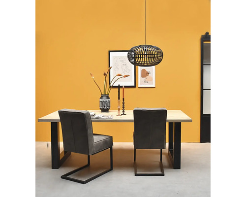 Coin repas moderne avec table en bois, pieds noirs en U, deux chaises grises et suspension noire en métal devant un mur jaune.