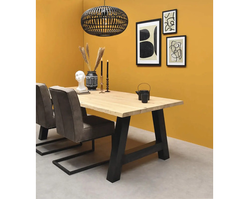 Salle à manger avec table en bois massif, pieds en métal noir, chaises rembourrées grises et suspension cage noire devant un mur jaune.