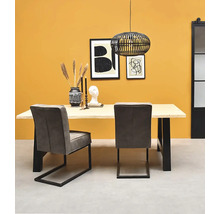 Salle à manger moderne avec table en bois clair, pieds en métal noir, chaises en tissu gris et suspension en fil de fer noir.