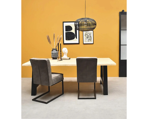 Salle à manger moderne avec table en bois clair, pieds en métal noir, chaises en tissu gris et suspension en fil de fer noir.