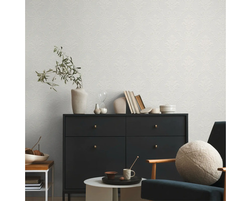 Dekoratives Zimmer mit gemusterter Tapete, Kommode, Sessel und Beistelltischen