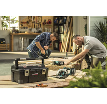 Werkstattszene mit Werkzeugkasten, Handkreissäge und zwei Handwerkern bei der Arbeit