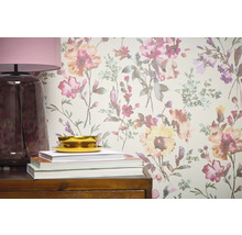 Gros plan d'un mur avec du papier peint à motifs floraux, complété par une lampe, des livres et un bol sur un meuble en bois.