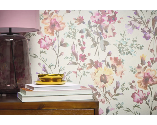 Gros plan d'un mur avec du papier peint à motifs floraux, complété par une lampe, des livres et un bol sur un meuble en bois.