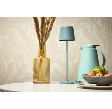 Nature morte décorative avec lampe de table, vase et thermos devant un papier peint à motifs.