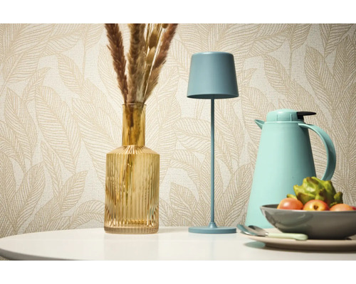 Nature morte décorative avec lampe de table, vase et thermos devant un papier peint à motifs.