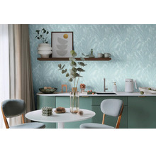 Pièce lumineuse avec table, chaises et kitchenette devant un mur avec du papier peint à motifs de feuilles.