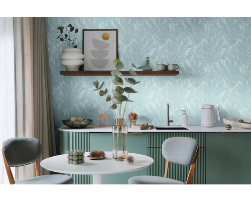 Pièce lumineuse avec table, chaises et kitchenette devant un mur avec du papier peint à motifs de feuilles.