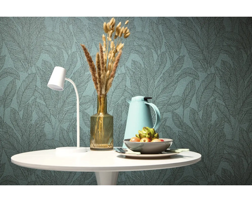 Table à manger décorative avec lampe, thermos, vase avec fleurs séchées et coupe de fruits devant un papier peint à motifs de feuilles