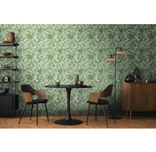 Salon avec table à manger, chaises, étagère, armoire et papier peint à motifs végétaux.