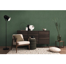 Salon avec fauteuil, lampadaire, commode et décorations devant un mur vert