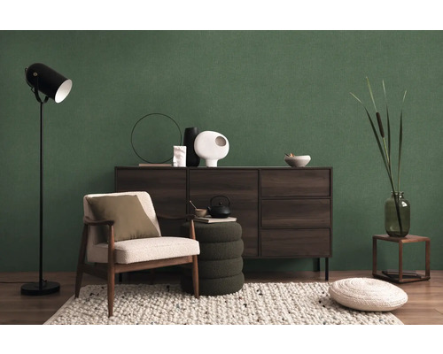 Salon avec fauteuil, lampadaire, commode et décorations devant un mur vert