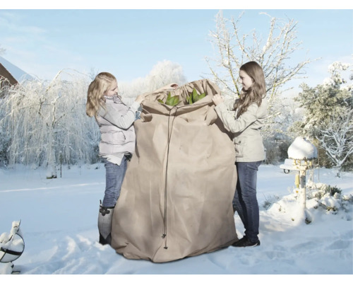 Deux personnes emballent des plantes dans un sac de protection hivernale dans un jardin enneigé.