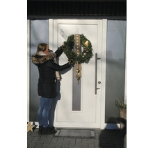 Une femme accroche une couronne de l'Avent décorée à une porte d'entrée.