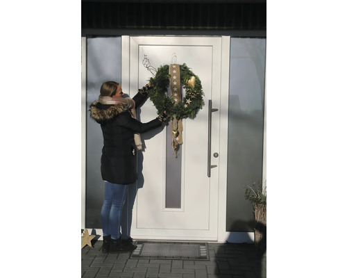 Une femme accroche une couronne de l'Avent décorée à une porte d'entrée.