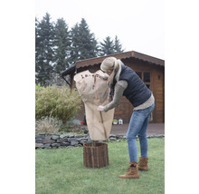Femme protège plante avec housse de protection hivernale dans le jardin.