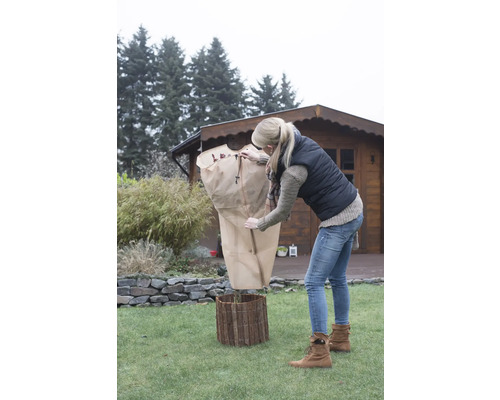 Femme protège plante avec housse de protection hivernale dans le jardin.
