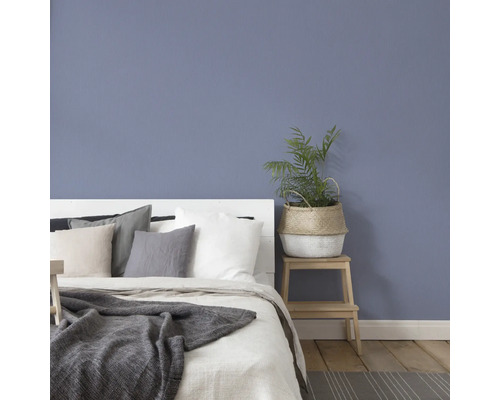 Schlafzimmer mit Bett, Kissen, Decke und Pflanze auf einem Hocker