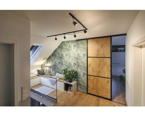 Lumineux appartement mansardé avec fenêtre de toit, coin salon, papier peint à feuilles vertes, porte coulissante et parquet.