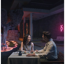 Un couple est assis à une table dans le jardin la nuit, éclairé par des rubans lumineux flexibles et une décoration en forme de cœur au néon.