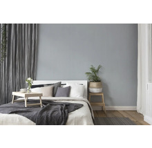 Helles Schlafzimmer mit Bett, Kissen, Decke, Beistelltisch und Zimmerpflanze